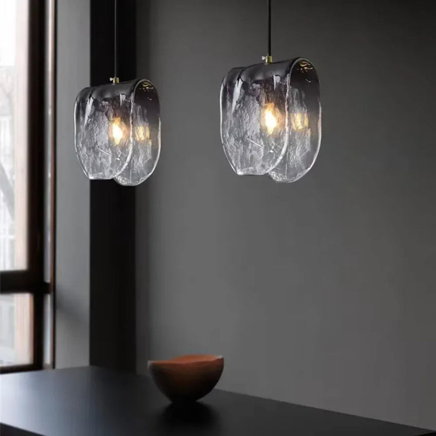 Two folded glass shades lit above a dark counter with a stone bowl