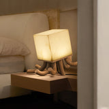 Sculptural table lamp lit on a nightstand beside a pale bed