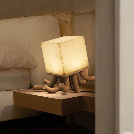 Sculptural table lamp lit on a nightstand beside a pale bed