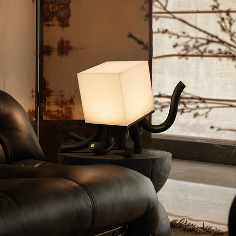 Sculptural table lamp lit beside a dark leather chair and branches