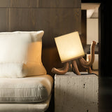 Sculptural table lamp lit beside a white armchair and a cushion