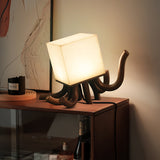Sculptural table lamp lit on a console below a framed artwork