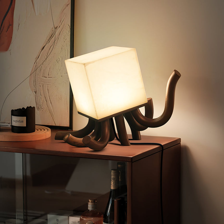 Sculptural table lamp lit on a console below a framed artwork