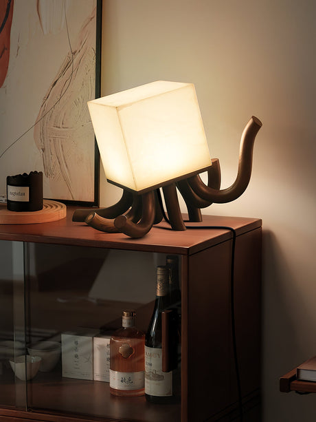 Sculptural table lamp lit on a red lacquered console in a dim room