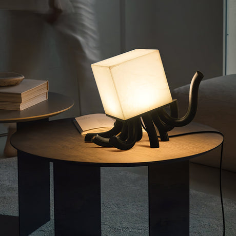 Sculptural table lamp lit on a round wood table with books