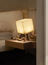 Sculptural table lamp lit on a floating shelf beside a headboard