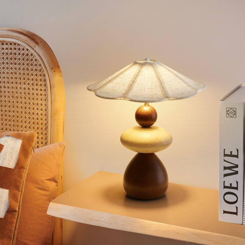 Sculptural table lamp lit on a pale shelf beside a standing book