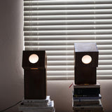 Two teak lamps lit on books in front of a window with blinds