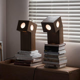 Two teak lamps lit on a wood desk beside stacks of books