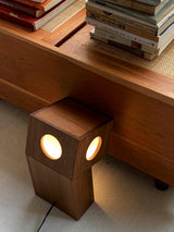 Teak lamp lit on the floor under a wood shelf holding books