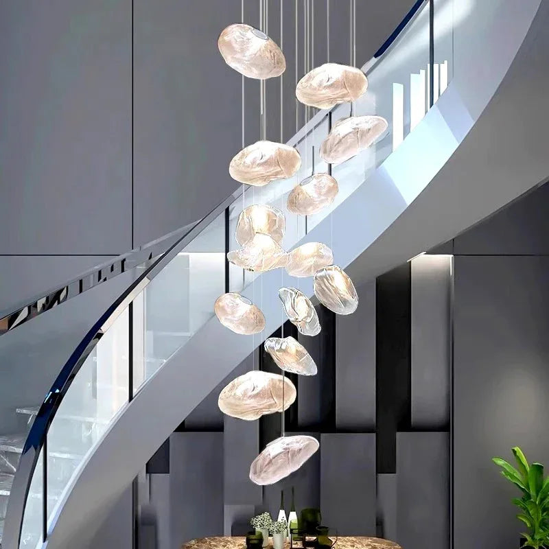 Cluster of amber glass shells lit above a curved white staircase in a tall hall