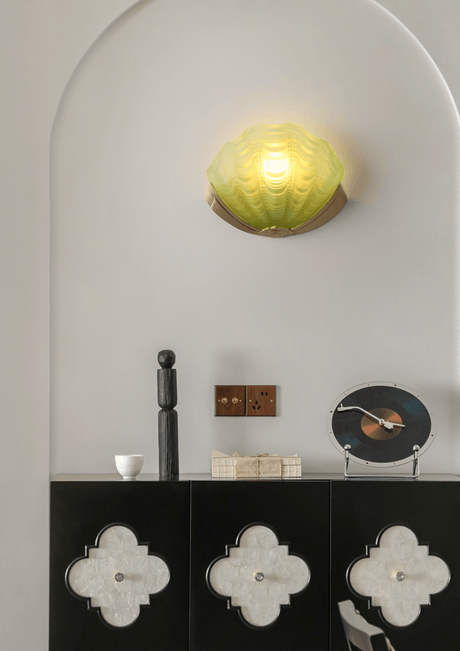 The green shell sconce lit inside an arched niche above a black cabinet