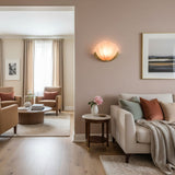 A shell sconce lit on a pink wall above a sofa, a side table and a rug