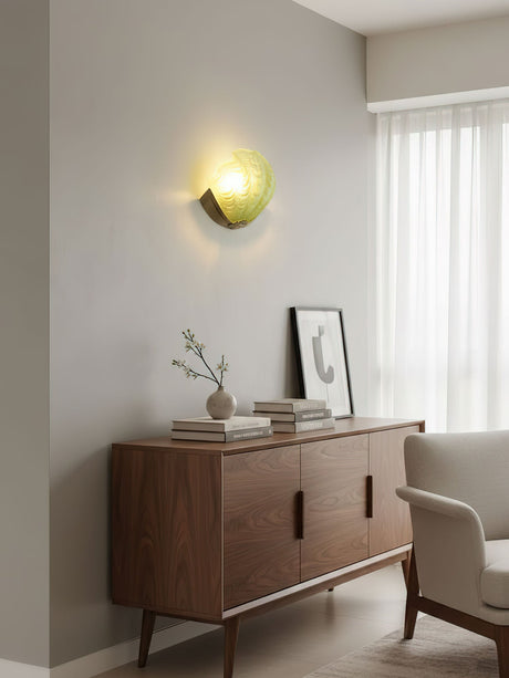 The green shell sconce lit above a walnut sideboard beside a window