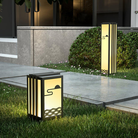 Two lit at the edge of a lawn beside pale paving and a concrete wall