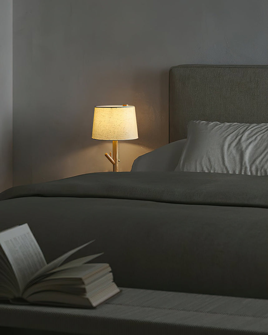 Branch stem lamp lit on a nightstand beside a bed and an open book