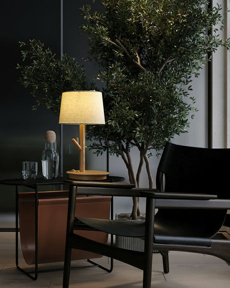 Branch stem lamp lit on a console beside a window and a potted olive tree