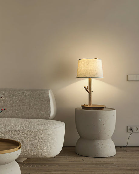 Branch stem lamp lit on a pale stone side table beside a low armchair