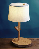 Branch stem side table lamp lit on a wood table against a deep blue wall