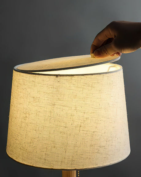 A hand resting on the top edge of the lit linen shade of the lamp