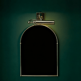 Polished tube lit above an arched black panel on a deep green wall
