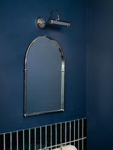 Chrome hooded bar lit above a tall arched mirror on a deep blue wall