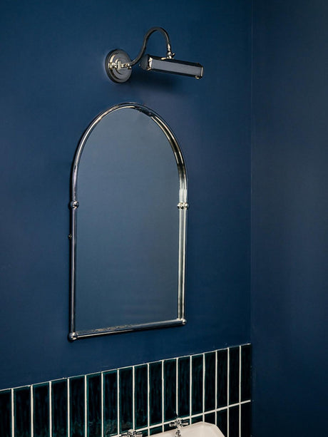 Chrome hooded bar lit above a tall arched mirror on a deep blue wall