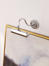 Chrome hooded bar lit above a gilt framed painting on a pale wall