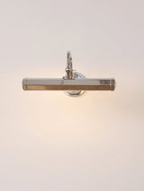 The chrome version lit on a pale wall, a hooded bar on a curved arm
