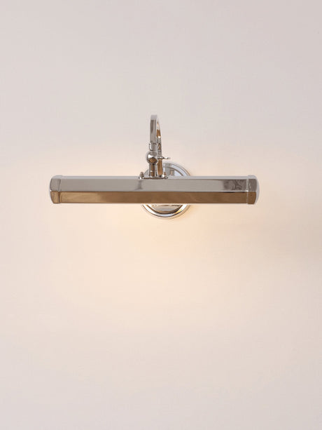The chrome version lit on a pale wall, a hooded bar on a curved arm