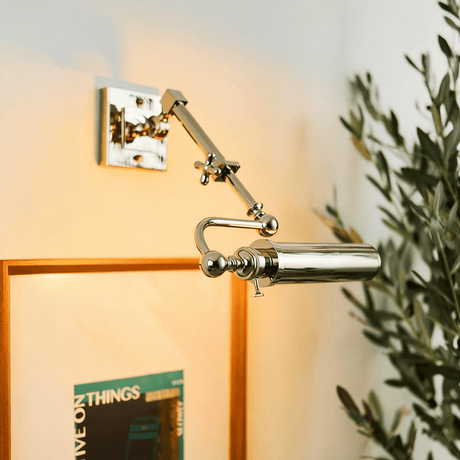 Polished tube lit over a framed print on a warm wall with olive foliage