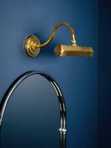 Gold hooded bar lit above an arched mirror on a deep blue painted wall