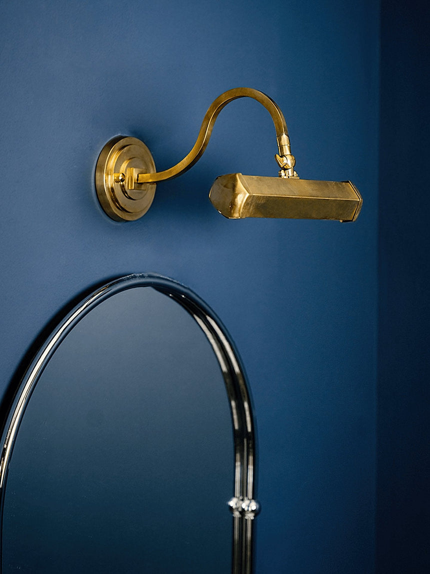 Gold hooded bar lit above an arched mirror on a deep blue painted wall