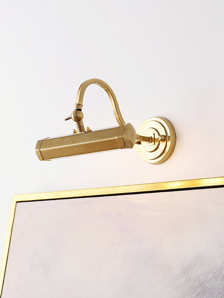 Gold hooded bar lit above a pale framed canvas on a white wall