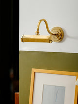 Gold hooded bar lit above a framed print in a dark green painted corner