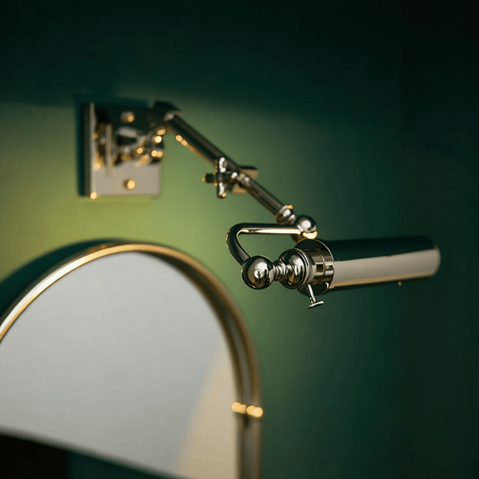 Polished tube lit beside an arched mirror on a deep green painted wall