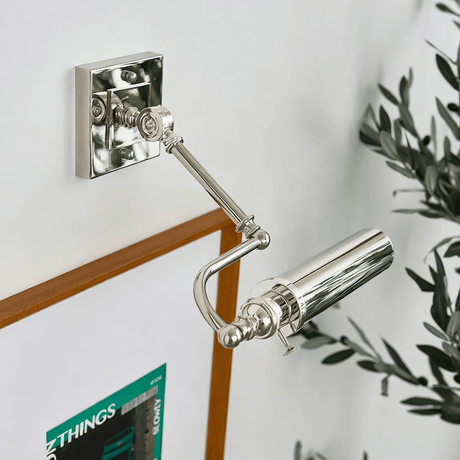Polished tube on a white wall lighting a framed print and olive branches