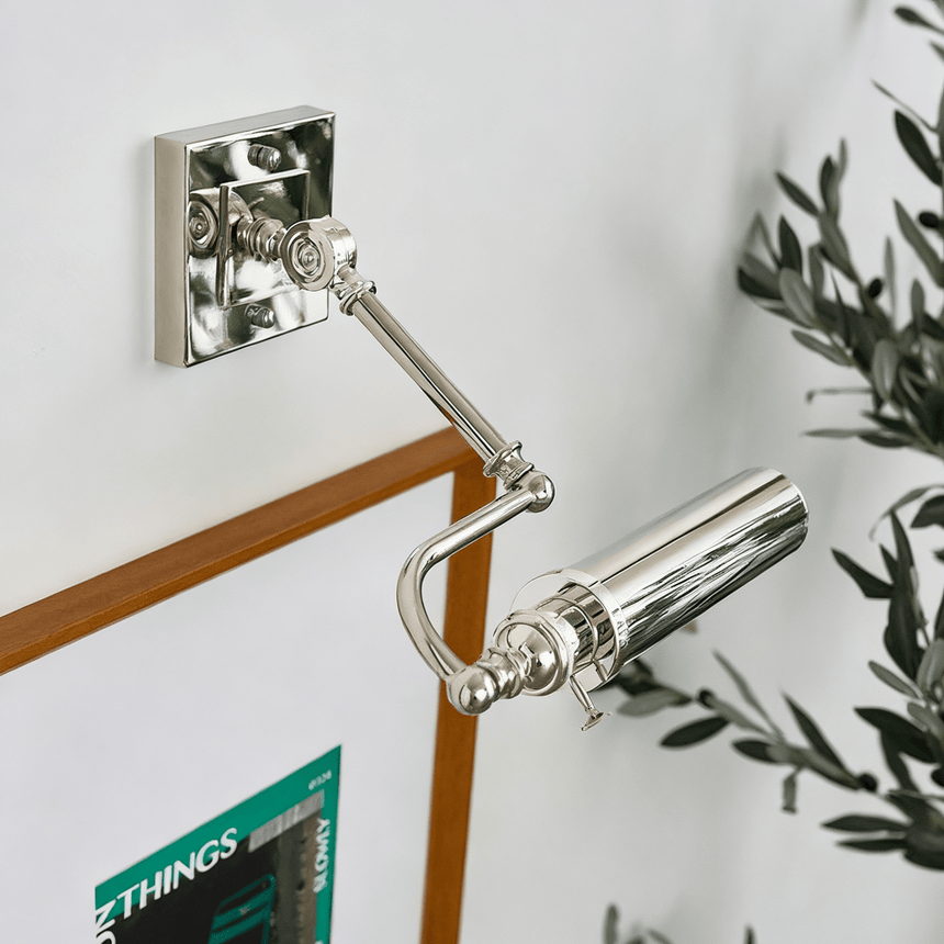 Polished tube on a white wall lighting a framed print and olive branches
