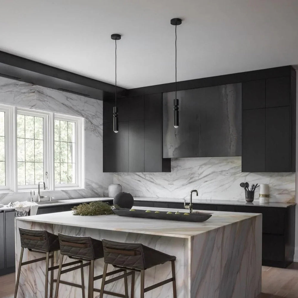 Two slim black tube pendants lit above a dark kitchen island