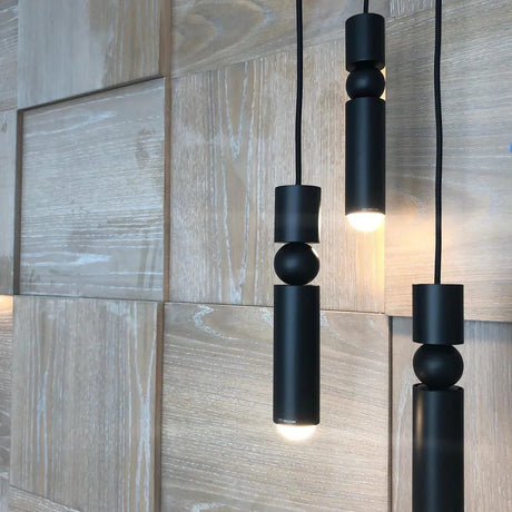 Three slim black tube pendants lit against a stone tiled wall