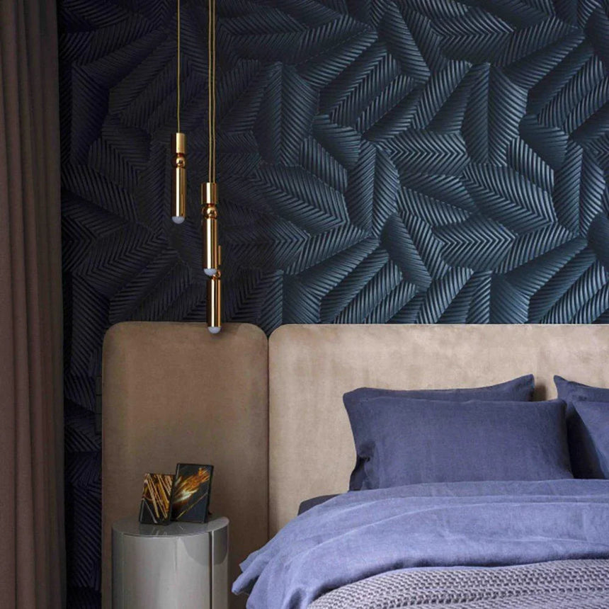 A slim gold tube pendant lit beside a bed with a padded headboard