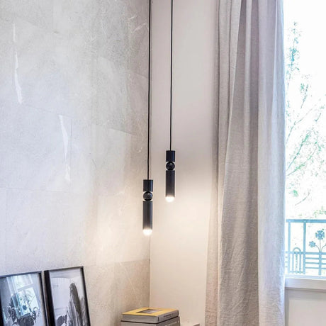 A slim gold tube pendant lit beside a long curtain and a framed picture