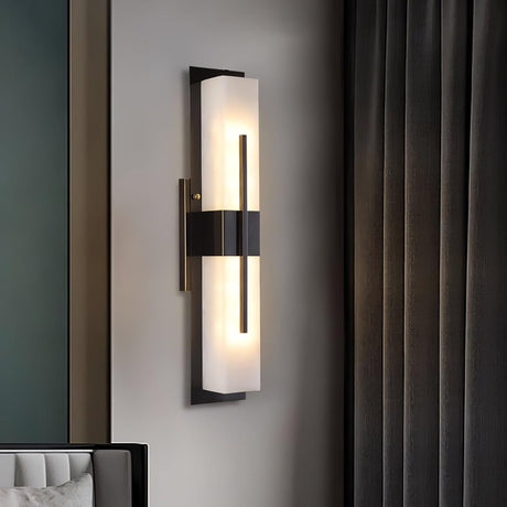 The sconce lit on a pale wall beside a dark green curtain and a chair