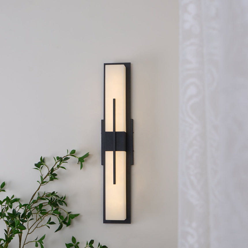 The sconce lit on a wall with trailing foliage crossing below it