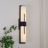 The sconce lit on a wall beside a linen curtain with leaves in front