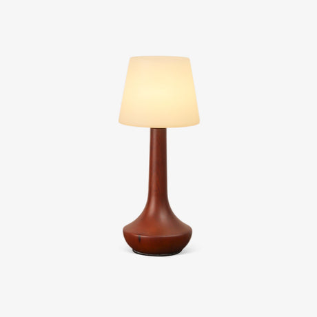 Small walnut lamp lit warm against a plain pale ground