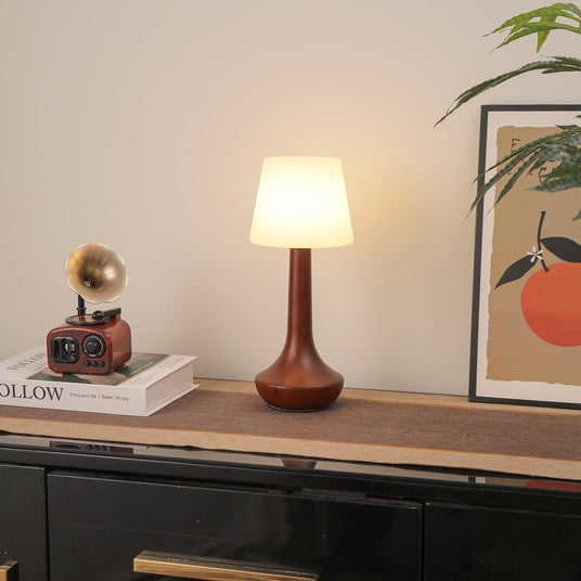 Small walnut lamp lit with a warm bulb on a wood shelf