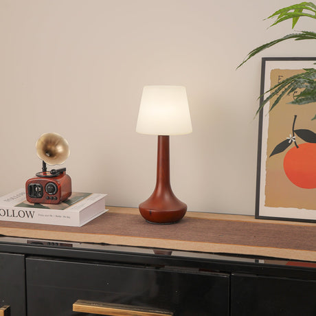 Small walnut lamp lit on a shelf beside a framed orange print