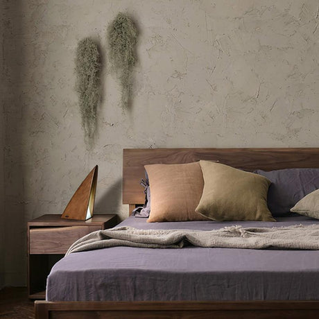 Small bedside lamp lit on a nightstand beside a made bed with cushions