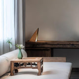 Small bedside lamp lit on a low carved table beside a pale sofa